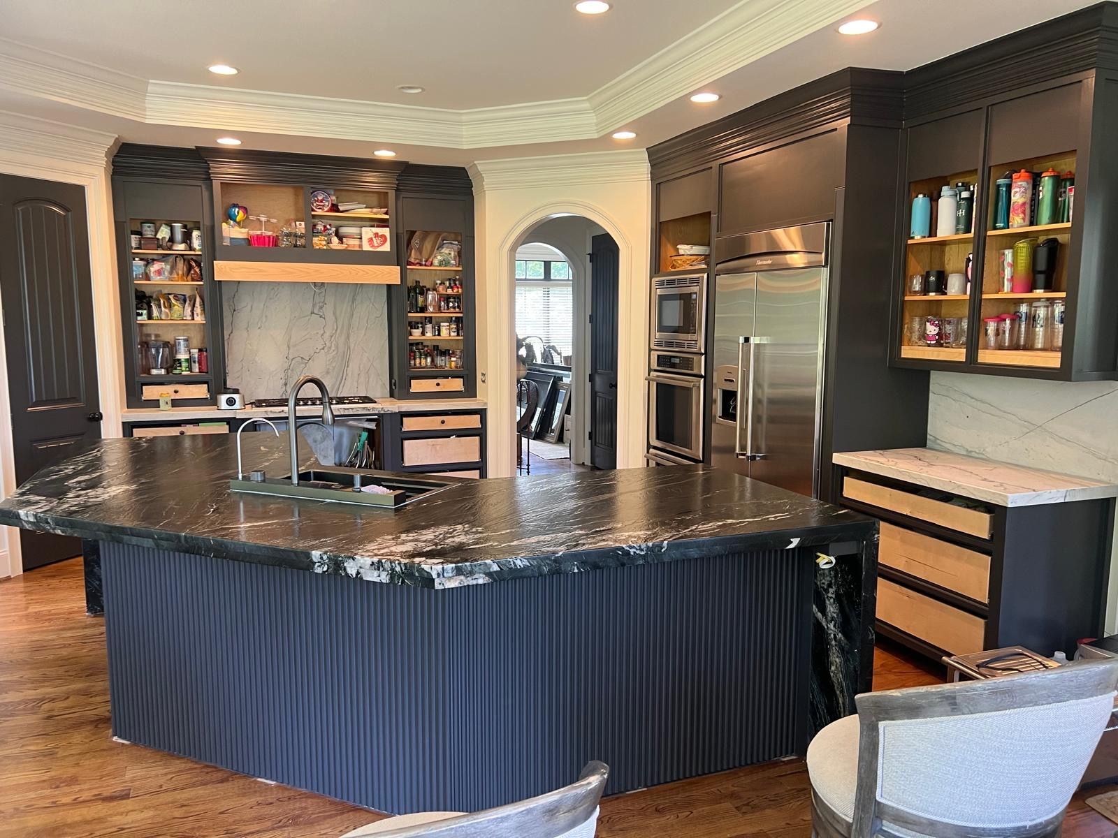 Luxurious kitchen with dark cabinetry, granite island, stainless steel appliances, and bar stools