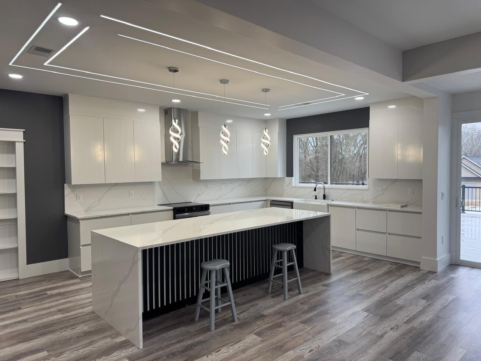 Modern white kitchen with island, pendant lights, wood floors, and a large window