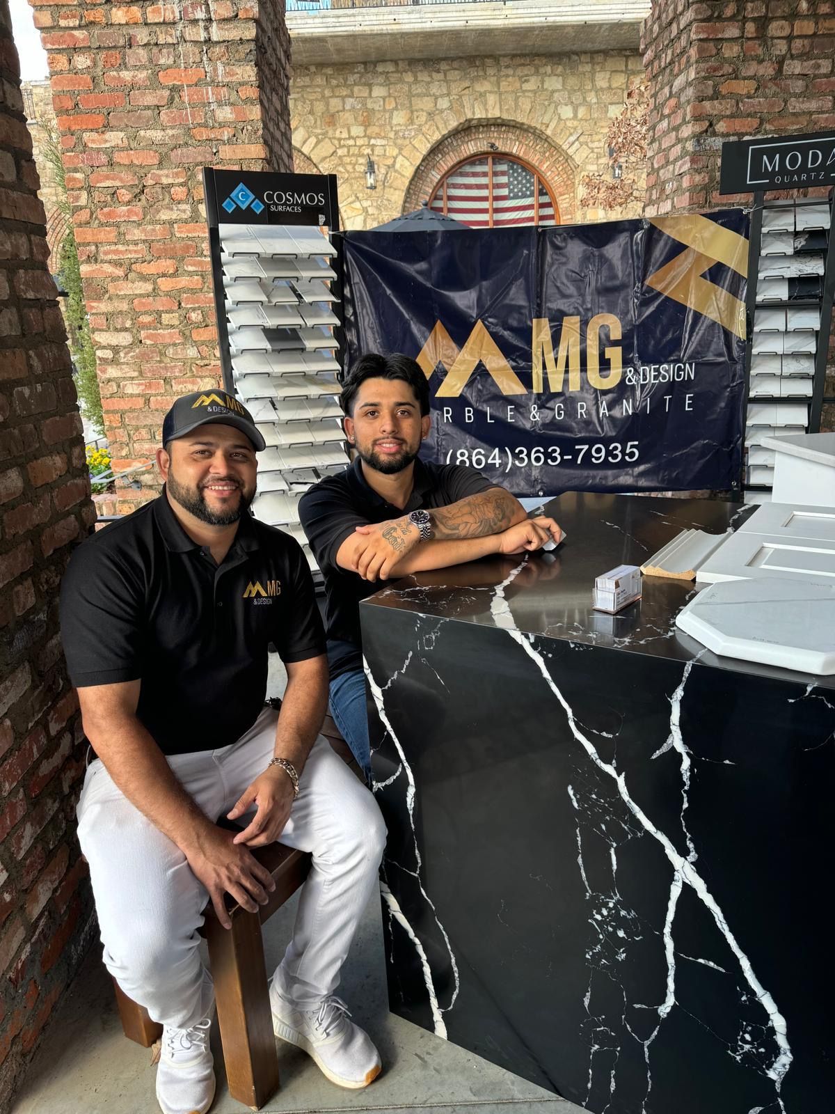 Two men behind a black marble-look counter in front of an AMG banner indoors