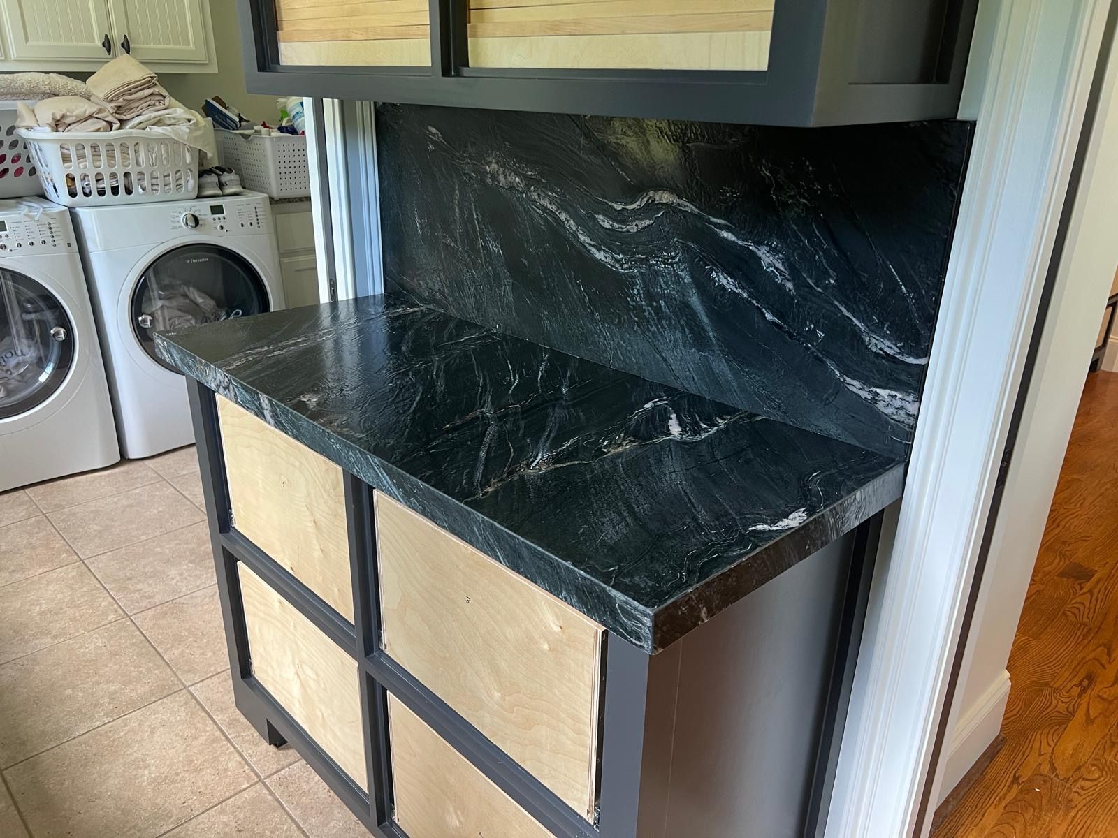 Laundry room counter with black marble top and beige cabinet fronts beneath a wall cabinet