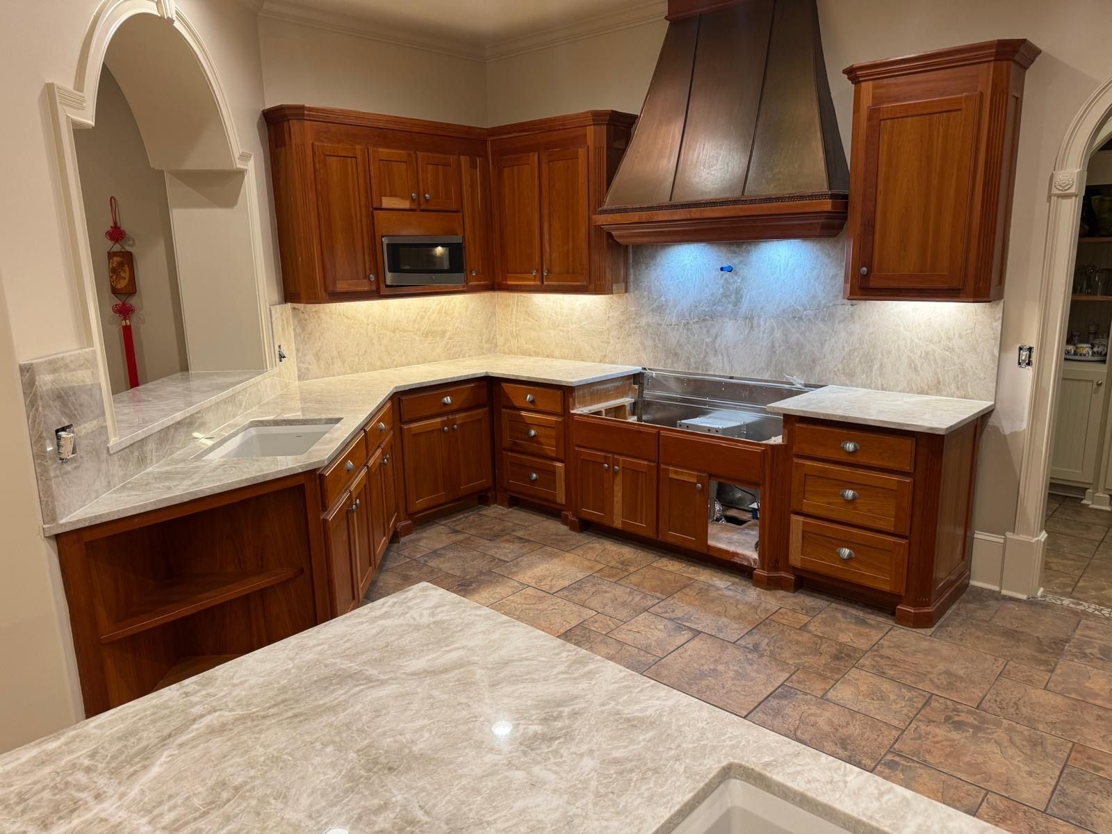 Warm-toned kitchen with wooden cabinets, marble countertops, and a stainless-steel range hood