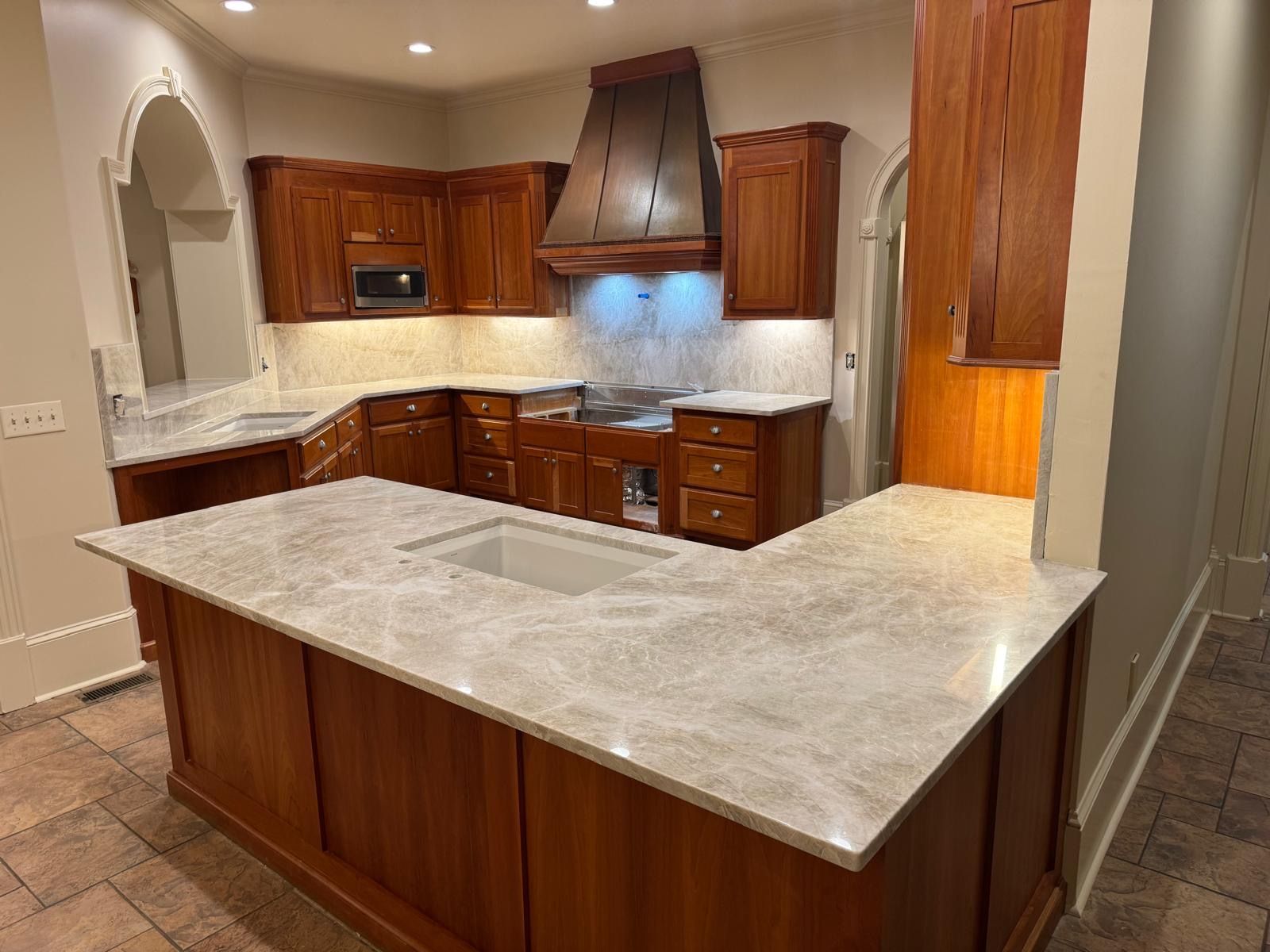 Wooden kitchen with gray countertops, central island, and range hood under warm lighting