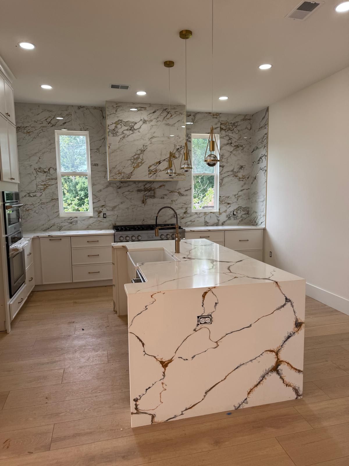 Modern kitchen with marble island, white cabinets, wood floor, and windows above the sink