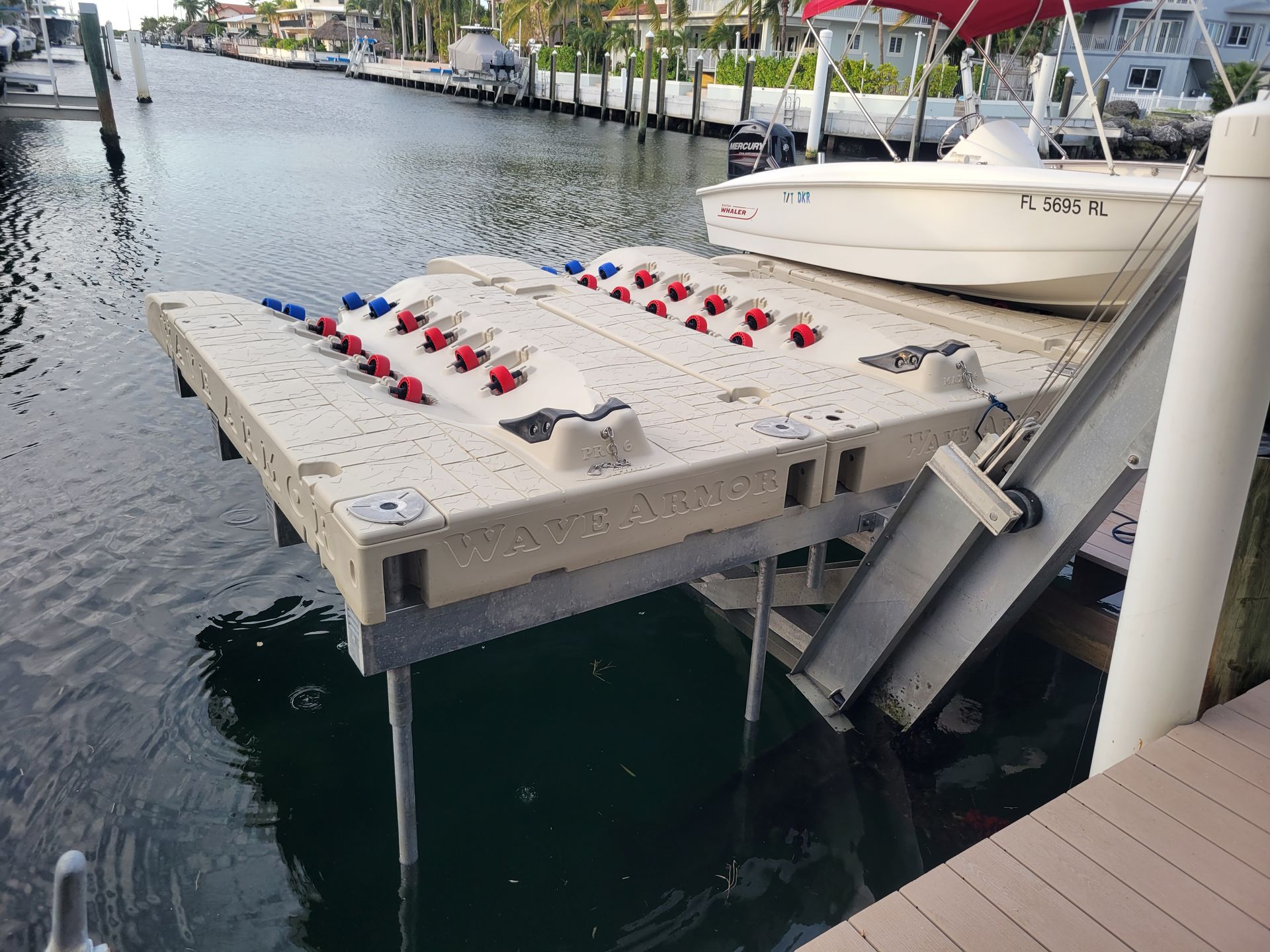 Dock with several red and blue boat bumpers, next to a white boat in a canal.