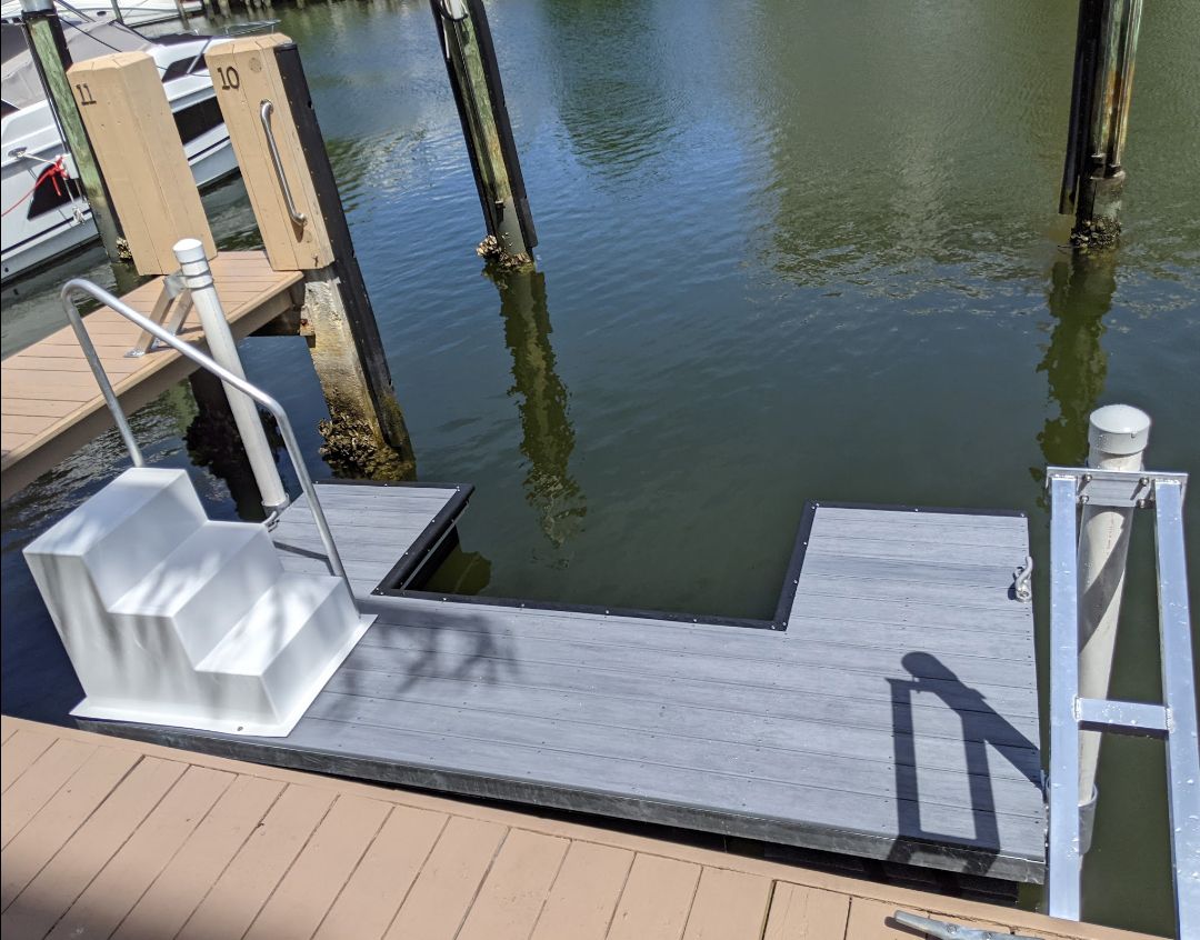 A dock extending into water with a staircase, with poles and railings, on a sunny day.
