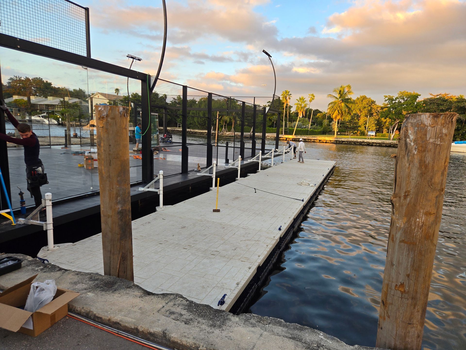 Dock extending into water with people, fencing, and construction materials.