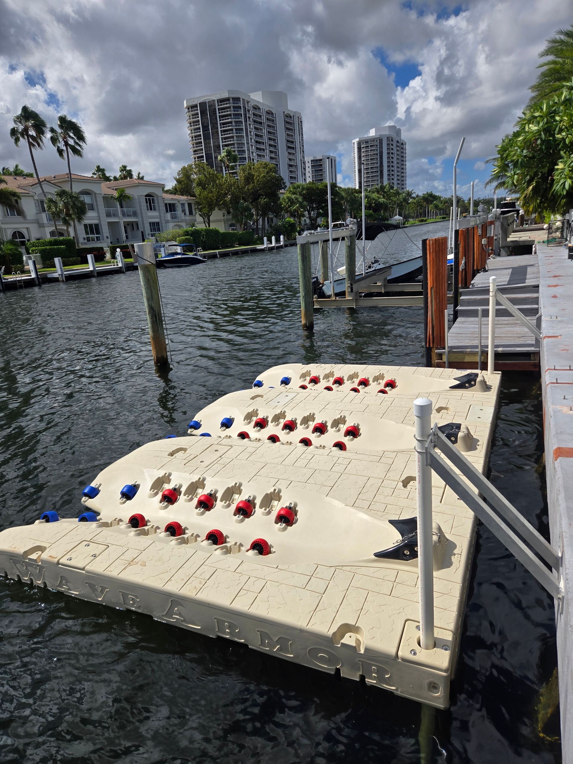 Floating dock with red/blue markers, on canal with buildings, cloudy sky.