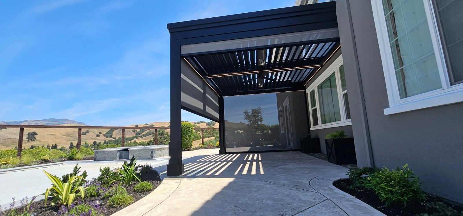 Modern house exterior with a covered patio, stone walkway, and landscaped garden under a blue sky