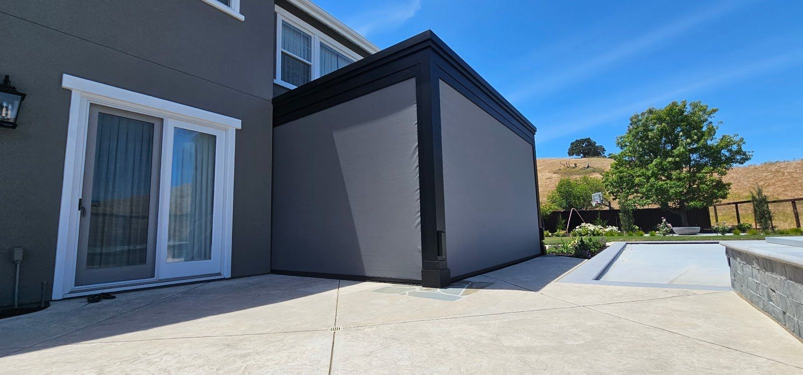 Patio beside a gray house and enclosed outdoor structure on a sunny day
