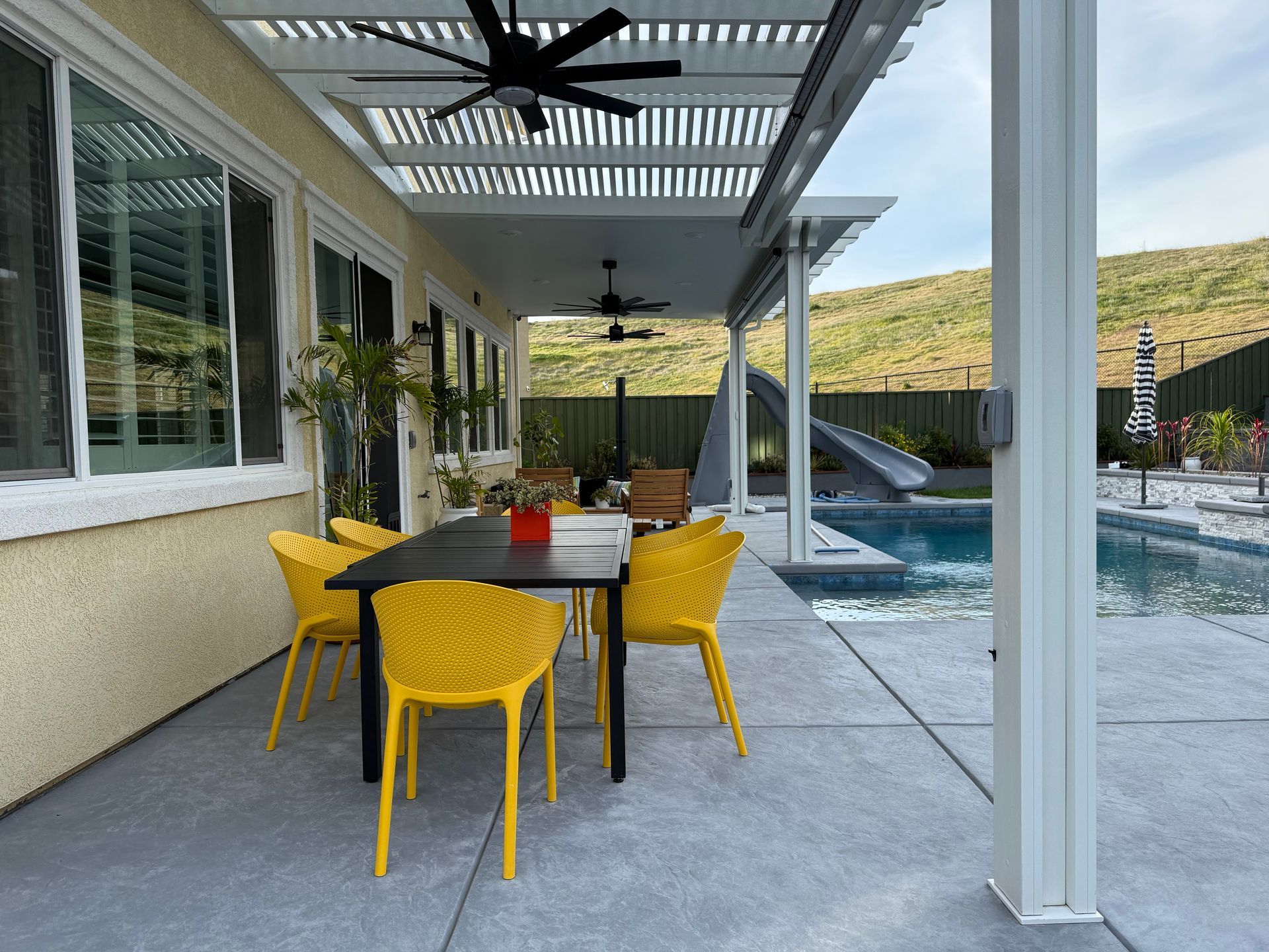 A patio with a table and chairs under a pergola next to a pool.