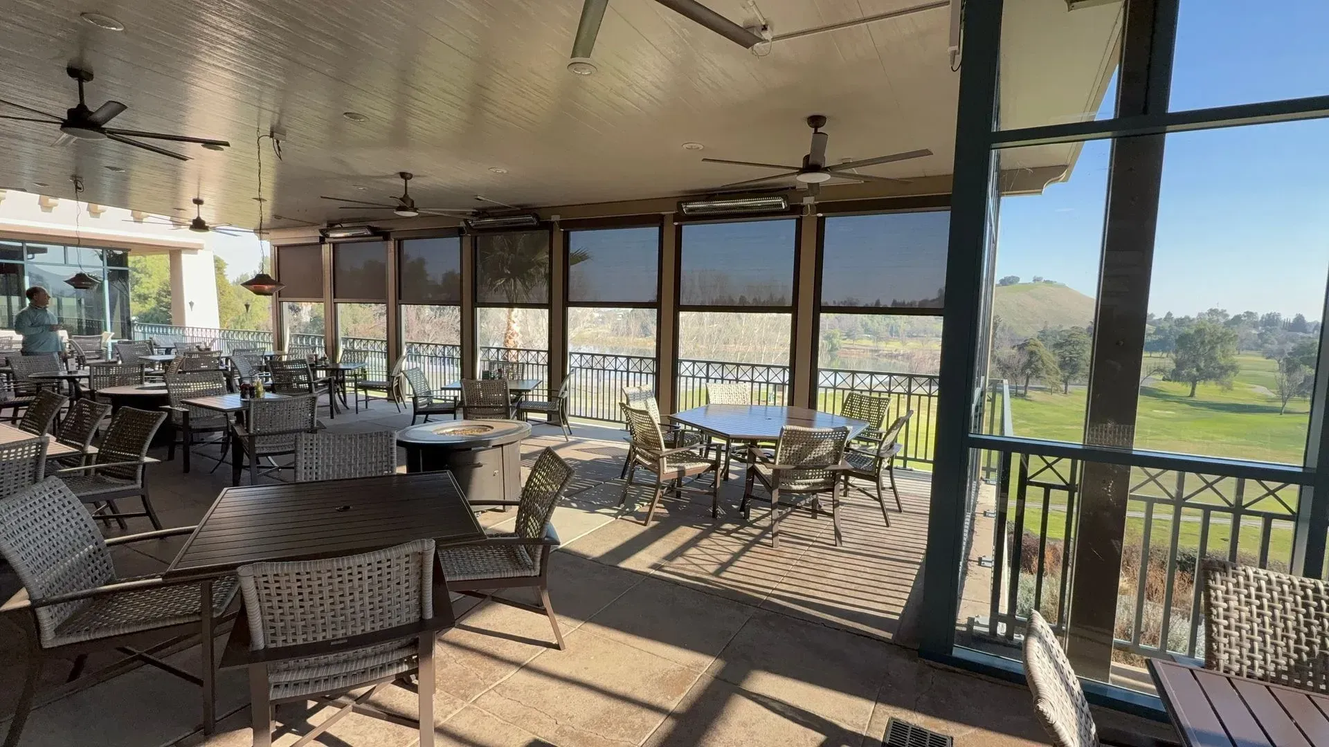 A screened in porch with tables and chairs and a view of a golf course.
