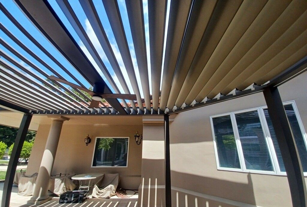 A person is standing under a pergola on a patio in front of a house.