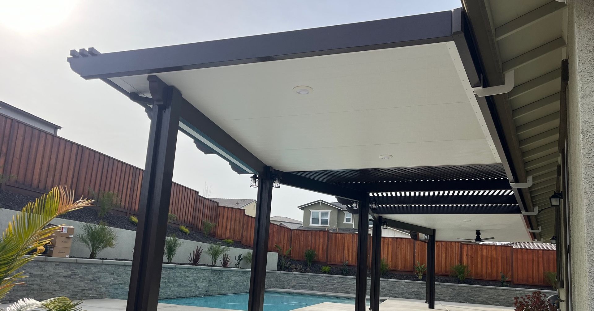 A pergola is sitting next to a swimming pool in a backyard.