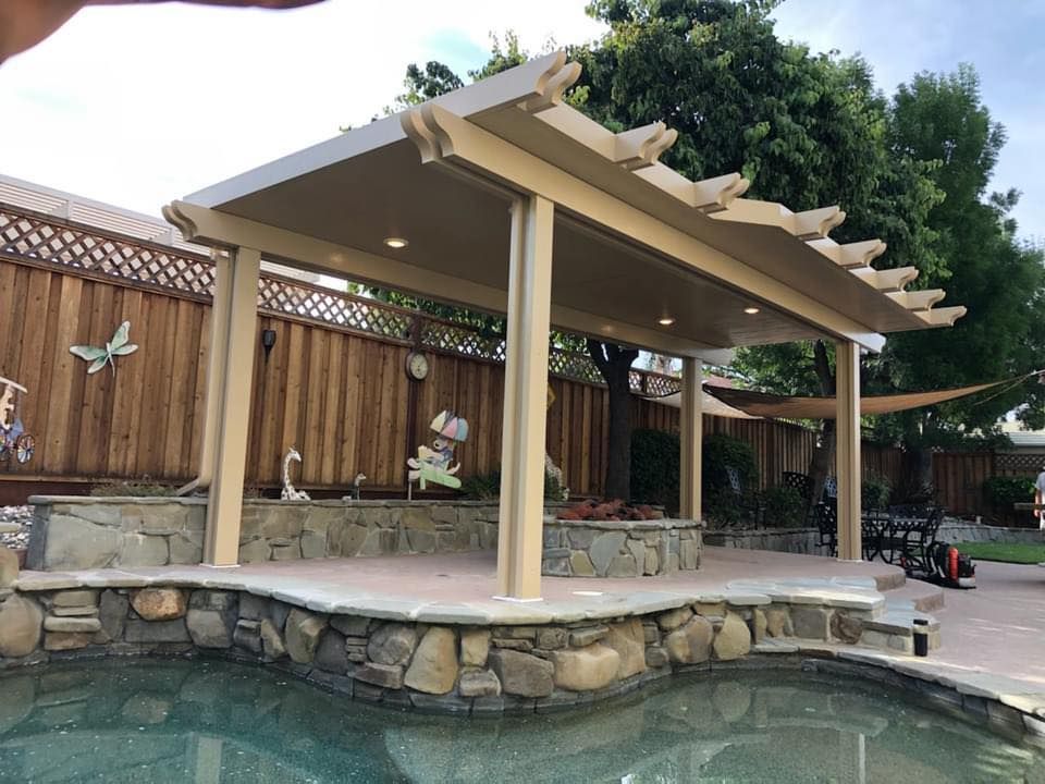 A pergola over a swimming pool with a wooden fence in the background.
