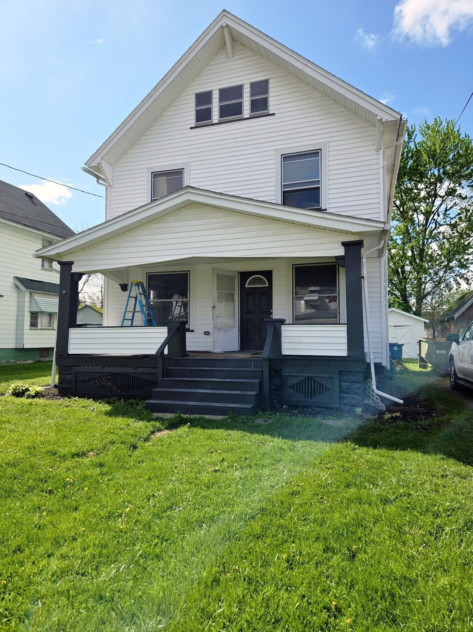 White two-story house with a front porch, black trim, and a green lawn under a blue sky
