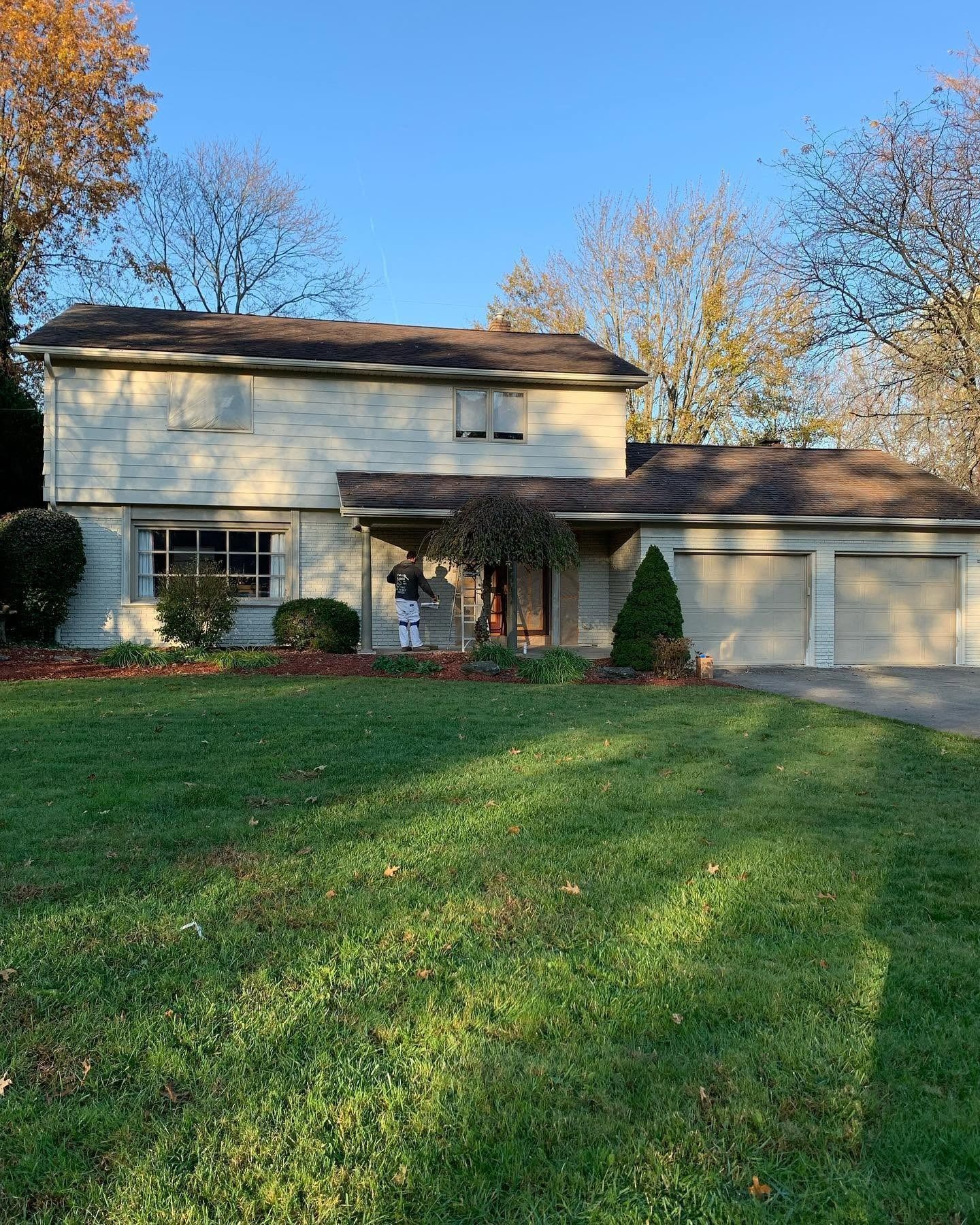 Suburban two-story house with beige siding, attached garage, and a green lawn in autumn sunlight
