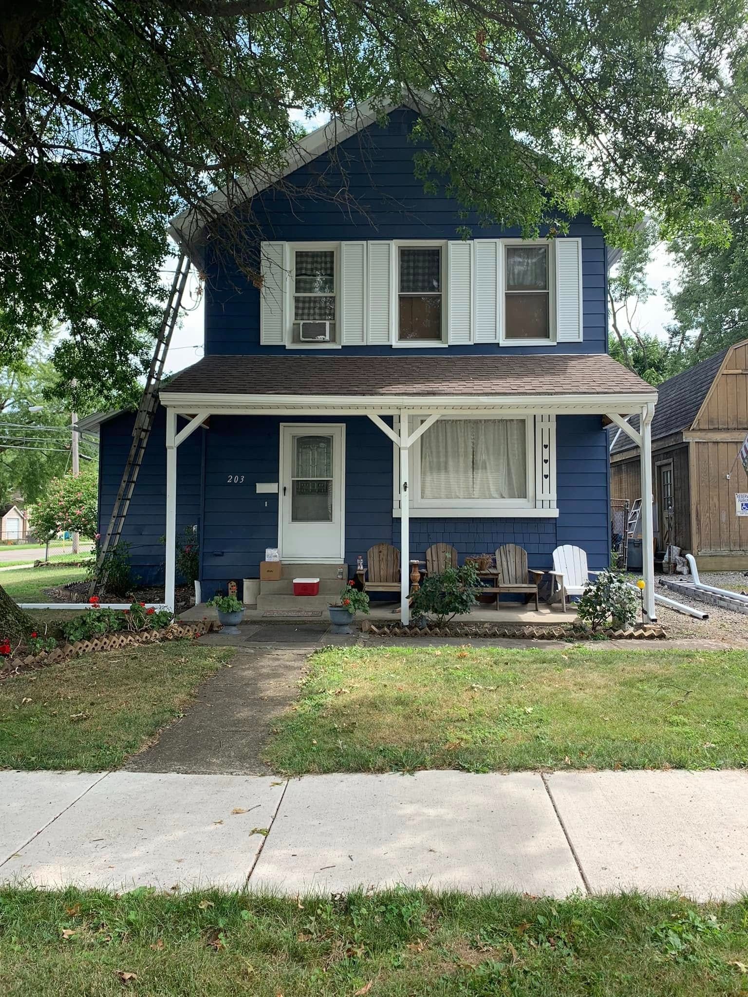 Blue two-story house with white trim, front porch, and a small front yard along a sidewalk.