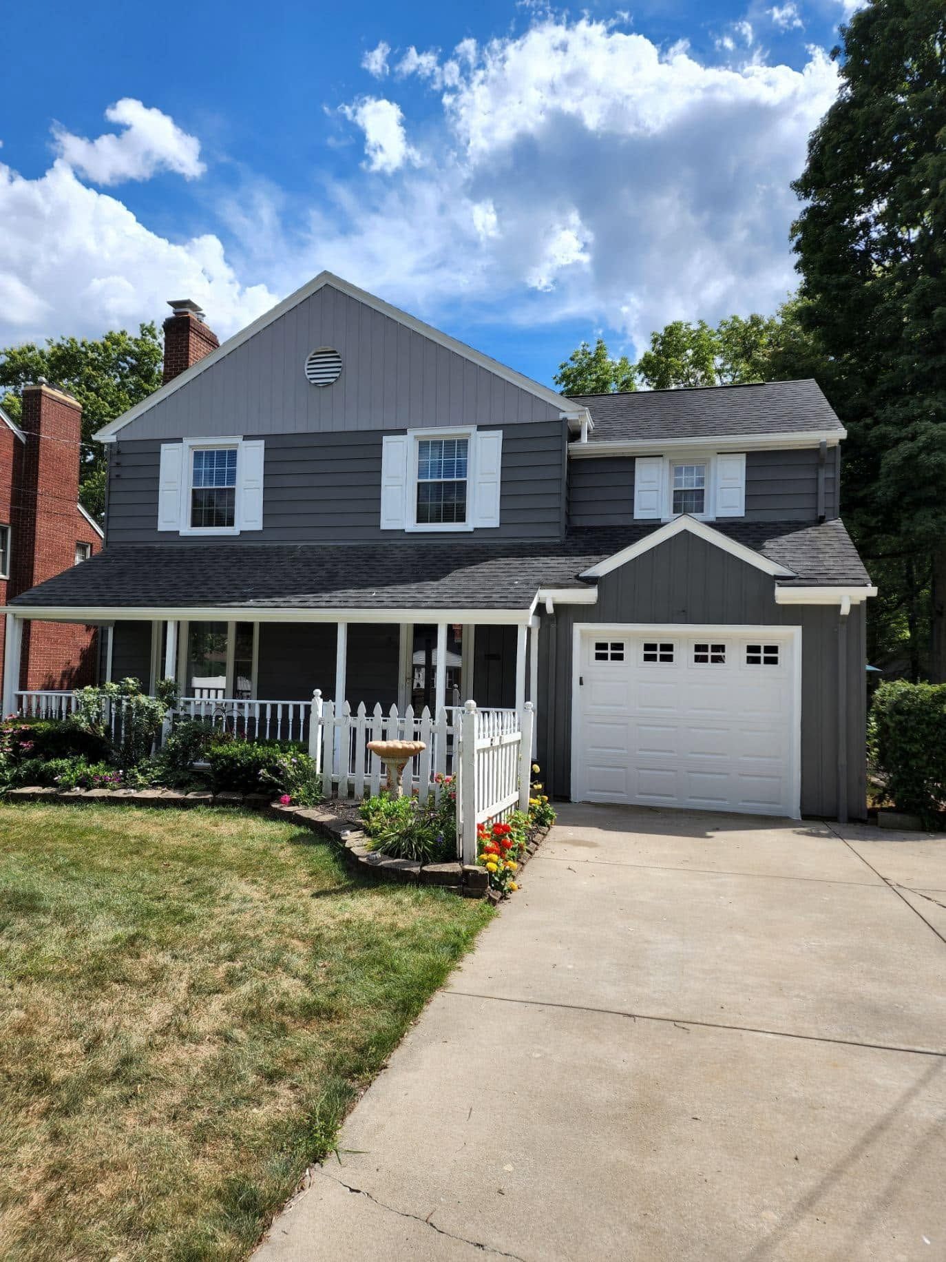 Gray two-story house with white trim, front porch, attached garage, and concrete driveway under a blue sky
