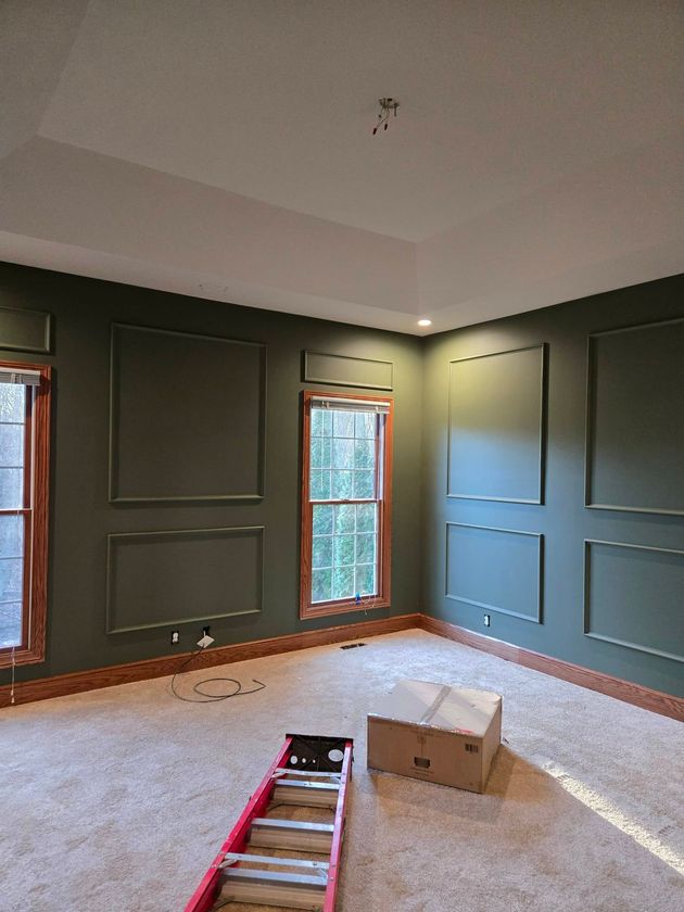 Empty room with dark green walls, carpet, windows, and a ladder and box on the floor.