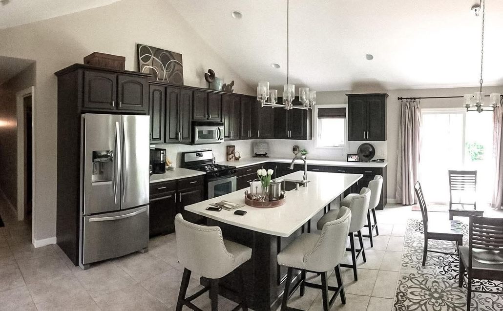 Modern kitchen with dark cabinets, stainless steel fridge, and a long island with stools and centerpiece.