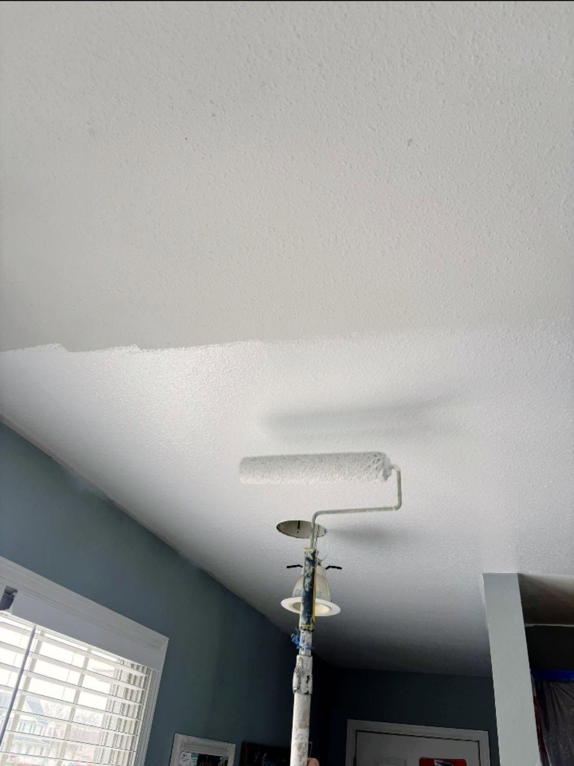 Ceiling being repainted white in a blue room, with painter’s pole and roller visible.