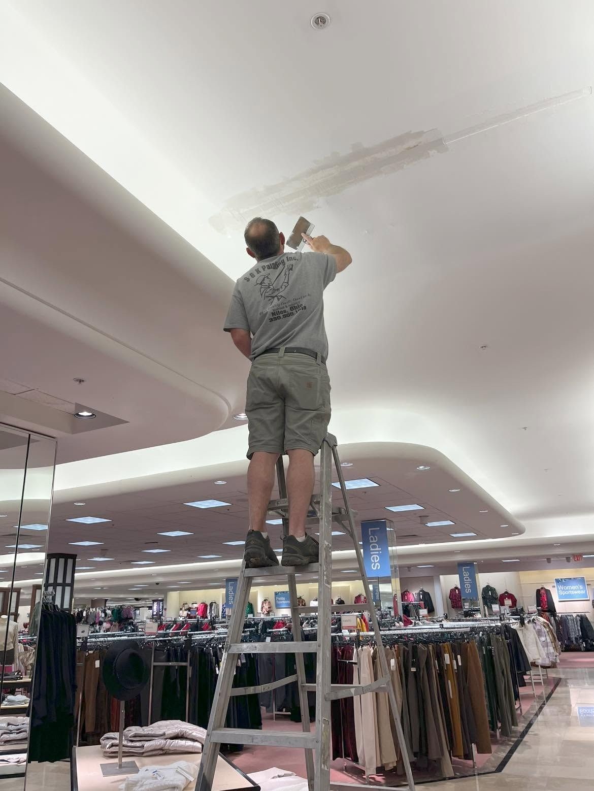 Worker on ladder painting the ceiling in a clothing store.