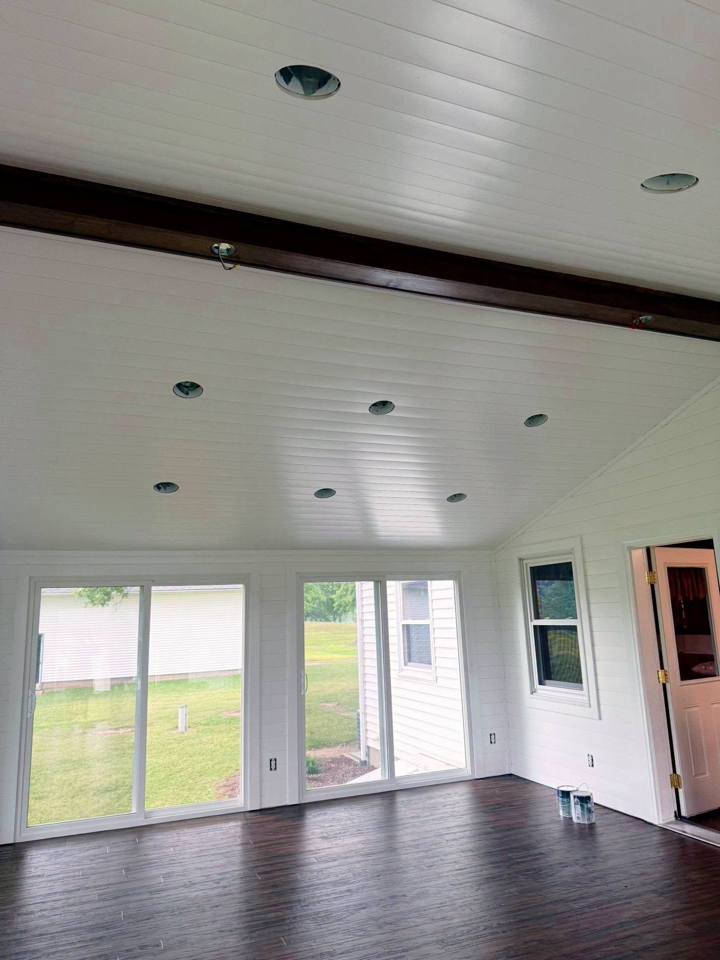 Empty white living room with dark wood floor, vaulted ceiling, and sliding glass doors overlooking a yard