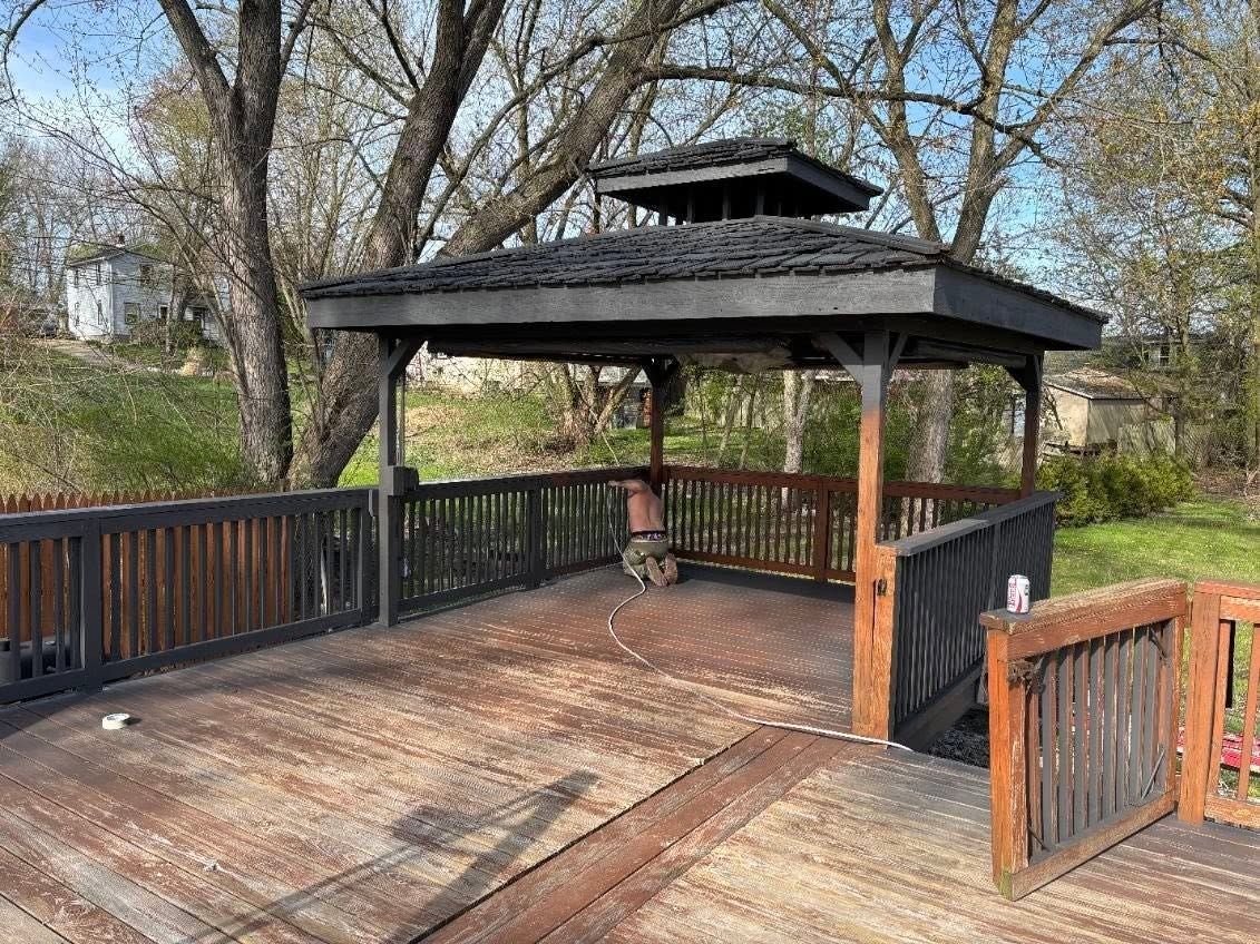 Wooden gazebo with dark railing and deck in a leafy park setting