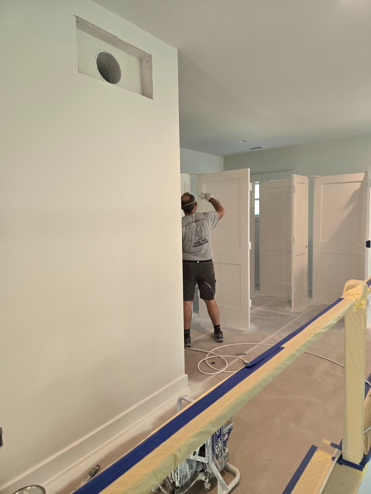 Person painting a hallway wall in a home under renovation, with protective coverings on the floor.