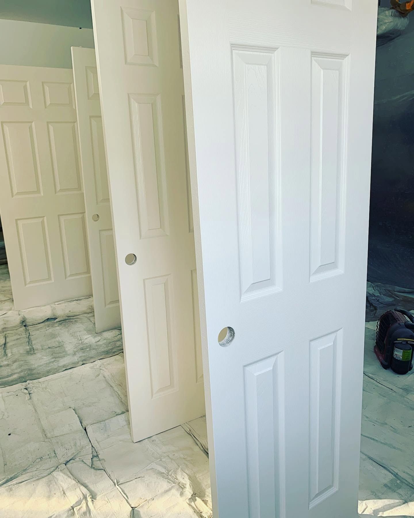 Three white interior doors leaning upright on a marble floor in a room under renovation