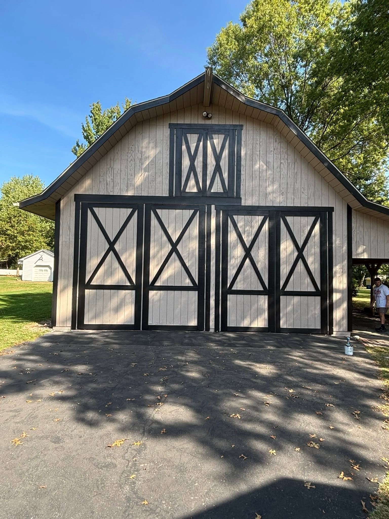 Barn with white siding, black trim, and three garage doors in a sunny driveway