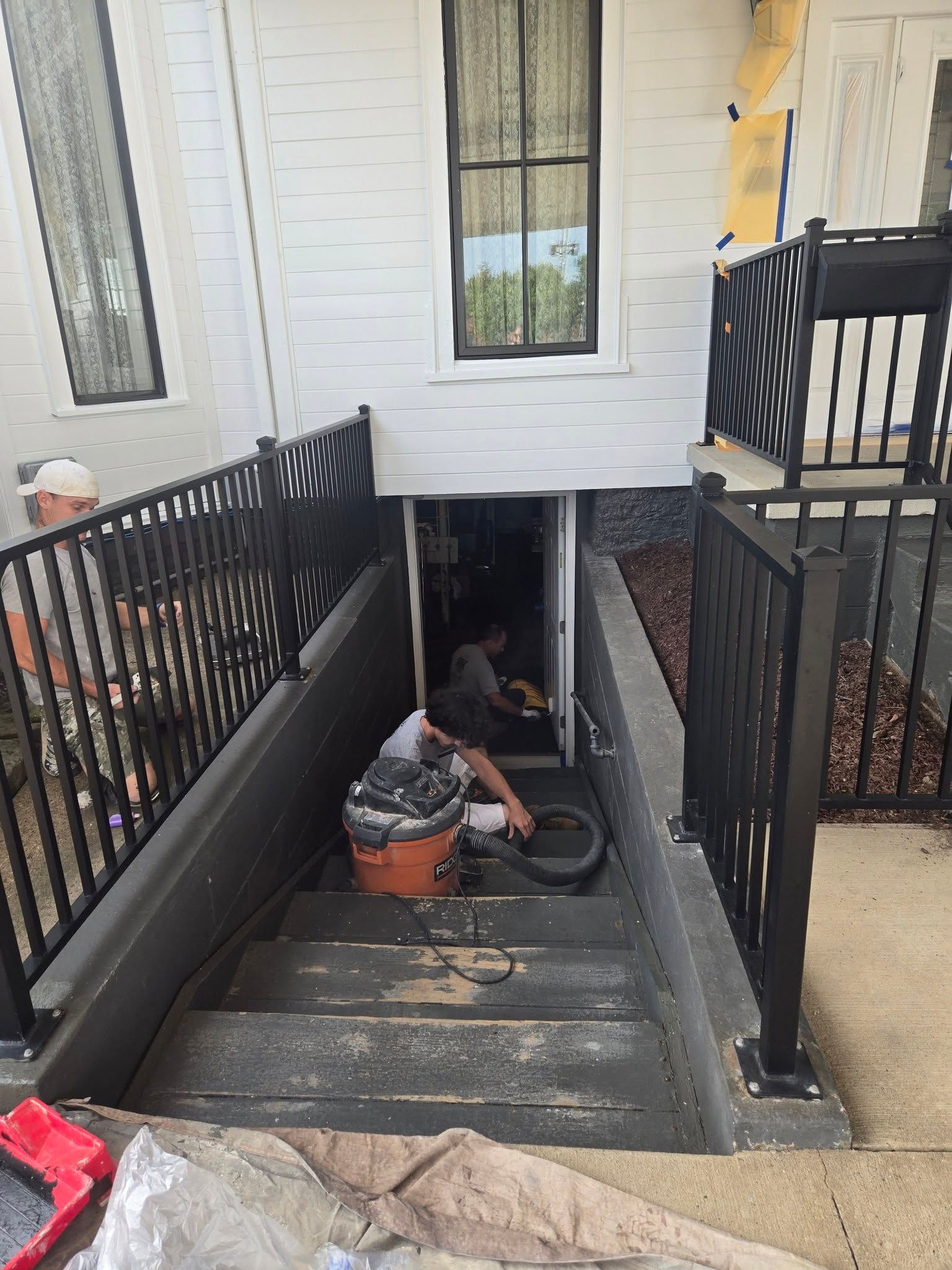 Worker using a wet vac on a basement stairwell below a porch entrance