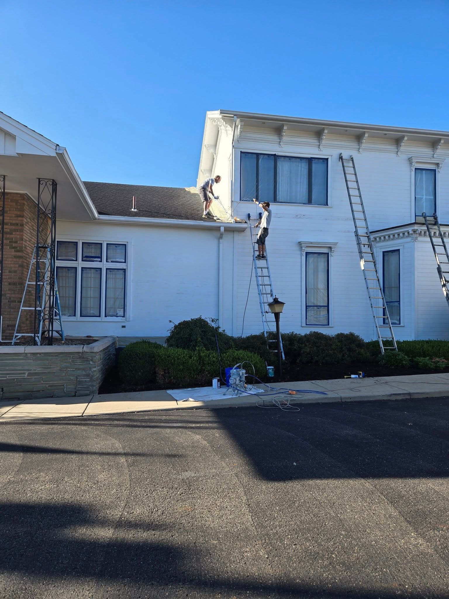 Damaged white building with cracked facade and two ladders leaning against it under a clear blue sky