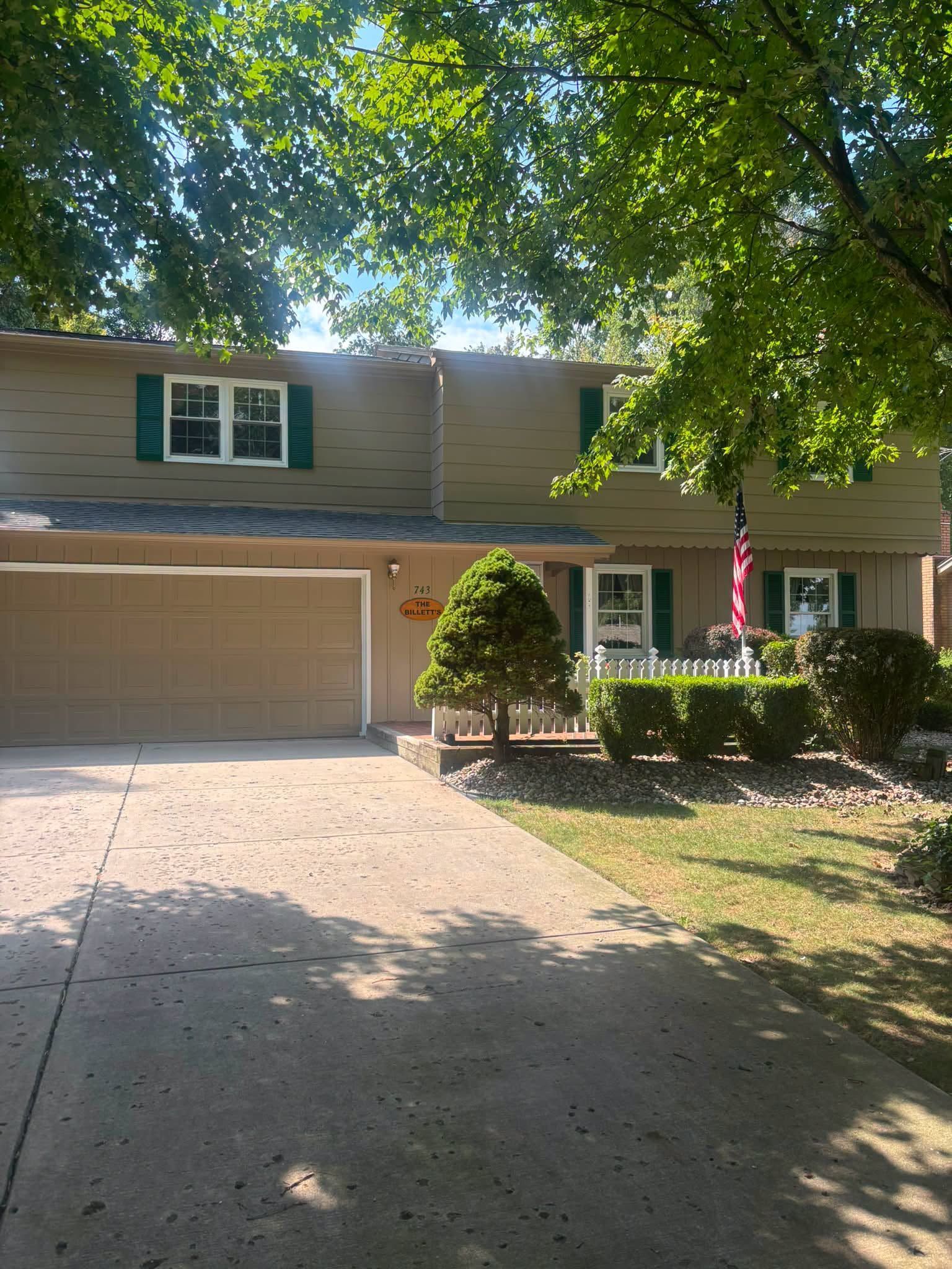Suburban house with two-car garage, brick driveway, and front yard shaded by trees