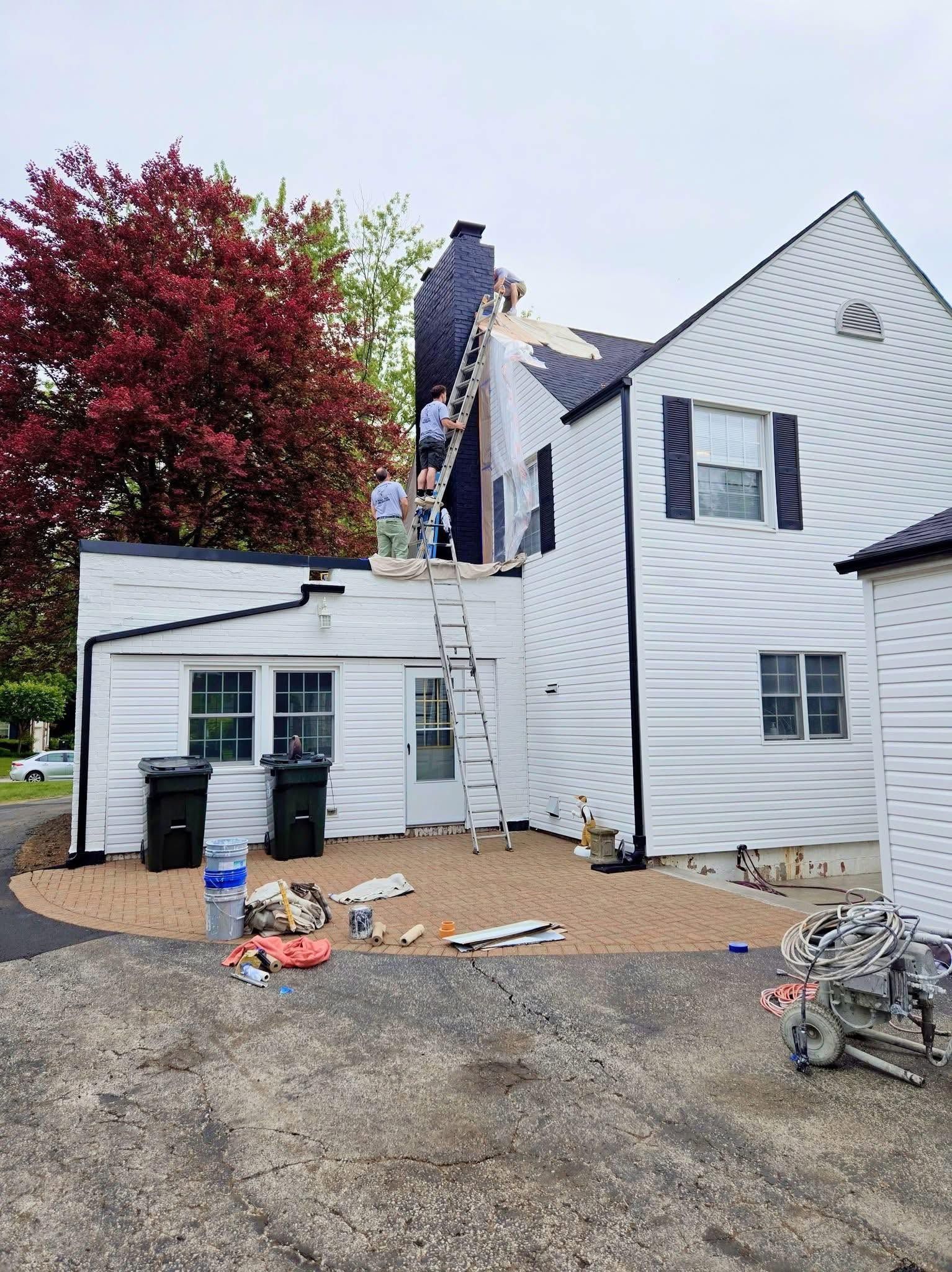 White house exterior with gravel driveway, scattered debris, and a large red tree beside it