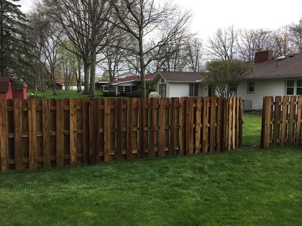 Wooden privacy fence in a grassy yard with houses and bare trees under an overcast sky