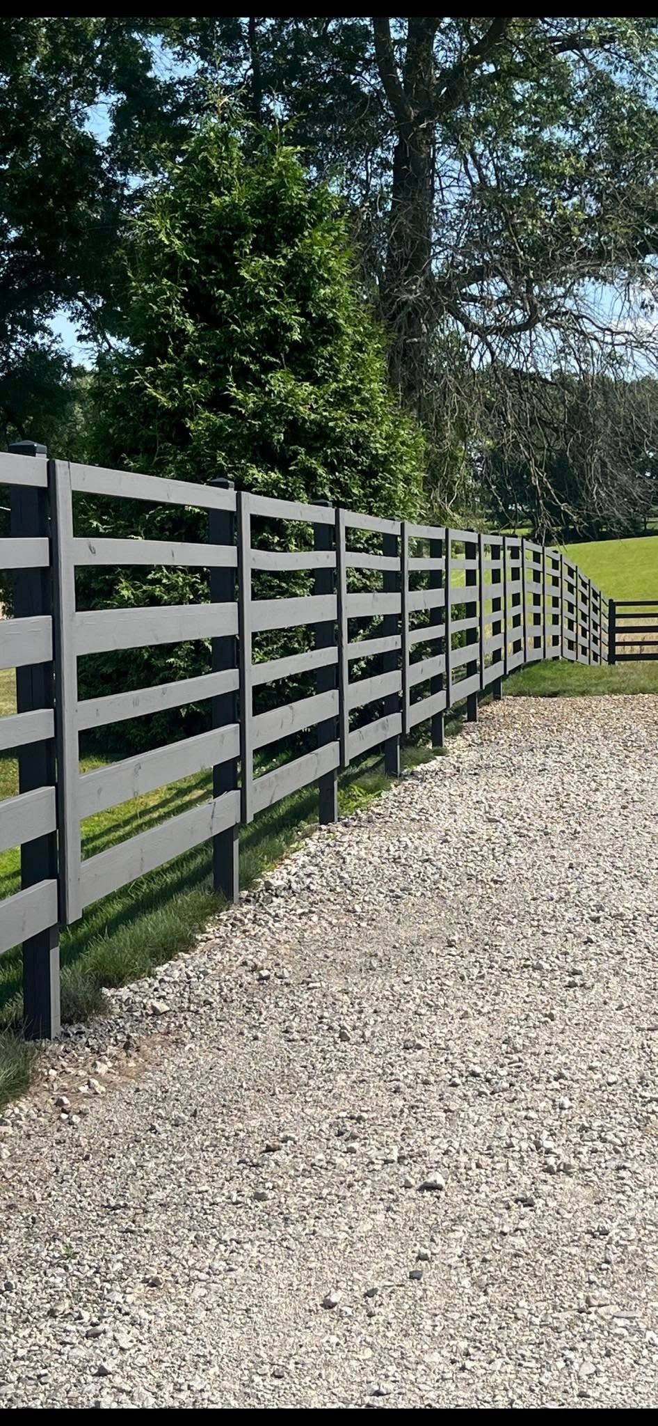 Gravel path beside a dark wooden fence with trees and greenery in the background