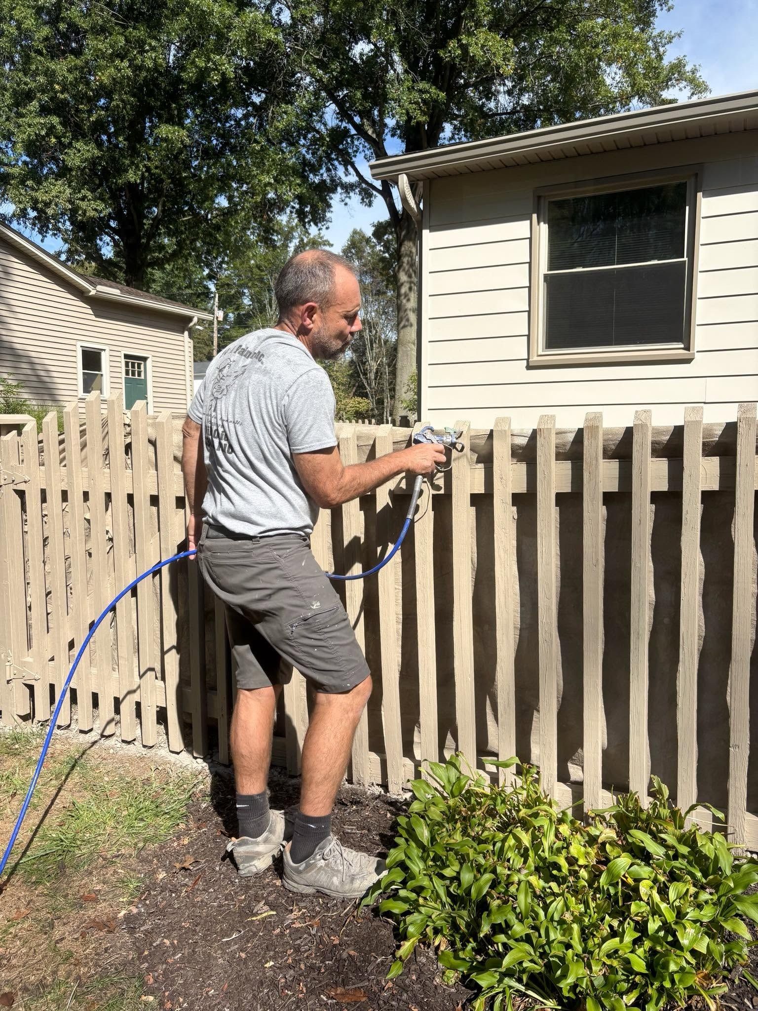 Man adjusting a wooden fence in a sunny backyard with a blue hose nearby