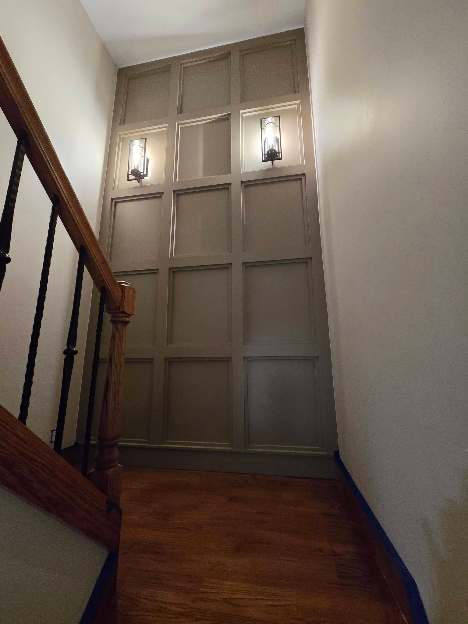 Narrow stair landing with wood floor, white walls, a wooden railing, and two wall sconces on a paneled wall