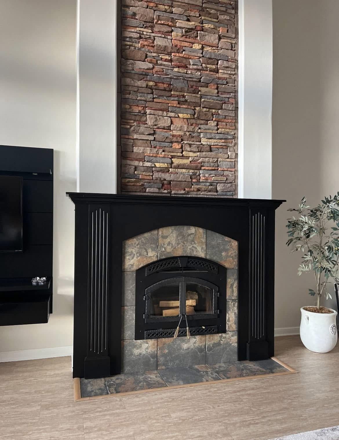 Modern living room fireplace with black mantel, brick surround, and a potted plant beside it
