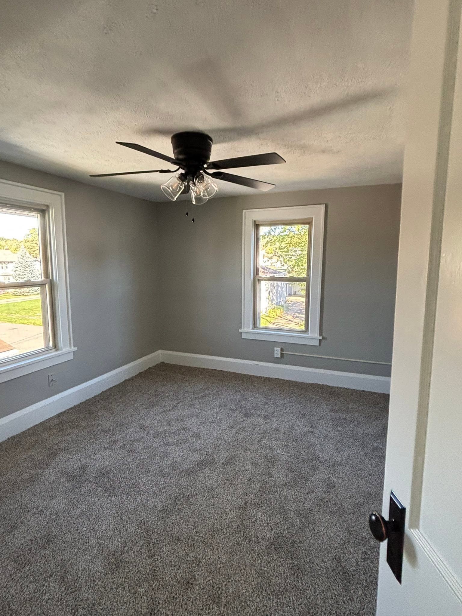 Empty carpeted bedroom with gray walls, two windows, and a black ceiling fan