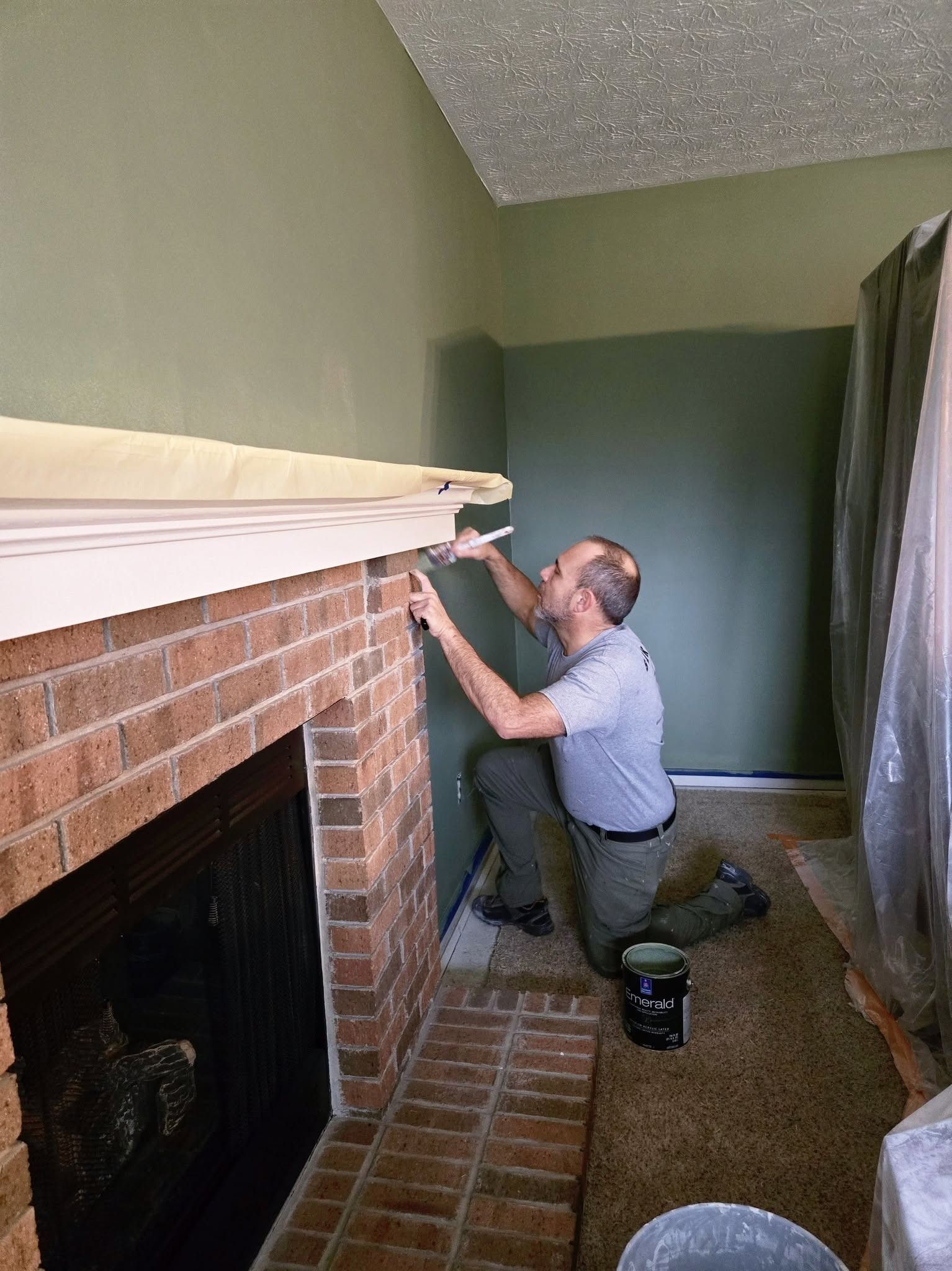Man kneeling by a brick fireplace, measuring and adjusting the mantel in a living room.