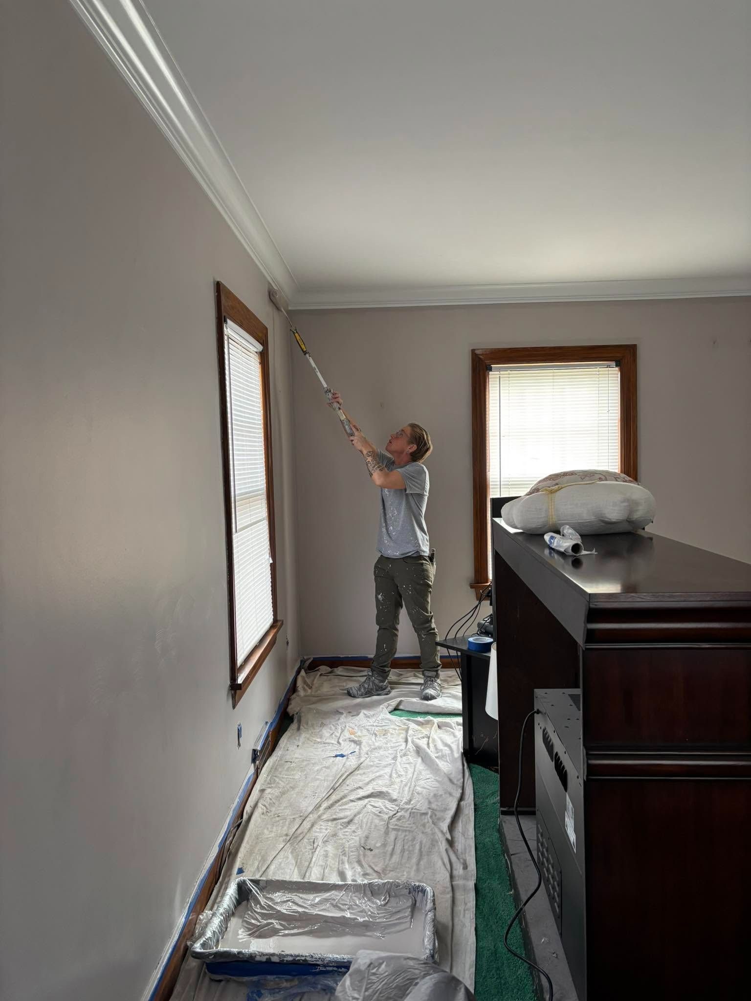 Person painting a gray ceiling in a room with protected floors and covered furniture.