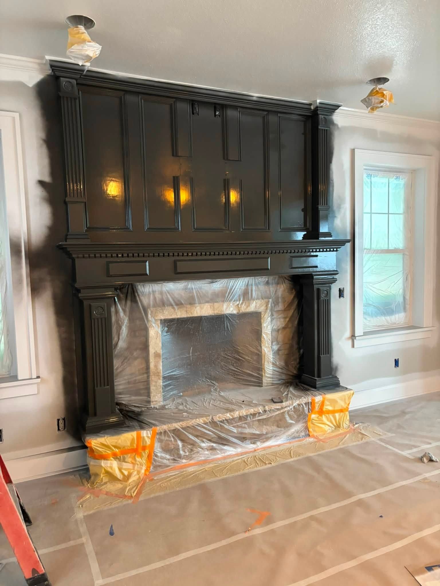 Black ornate fireplace mantle with mirrored tile surround in a room under renovation