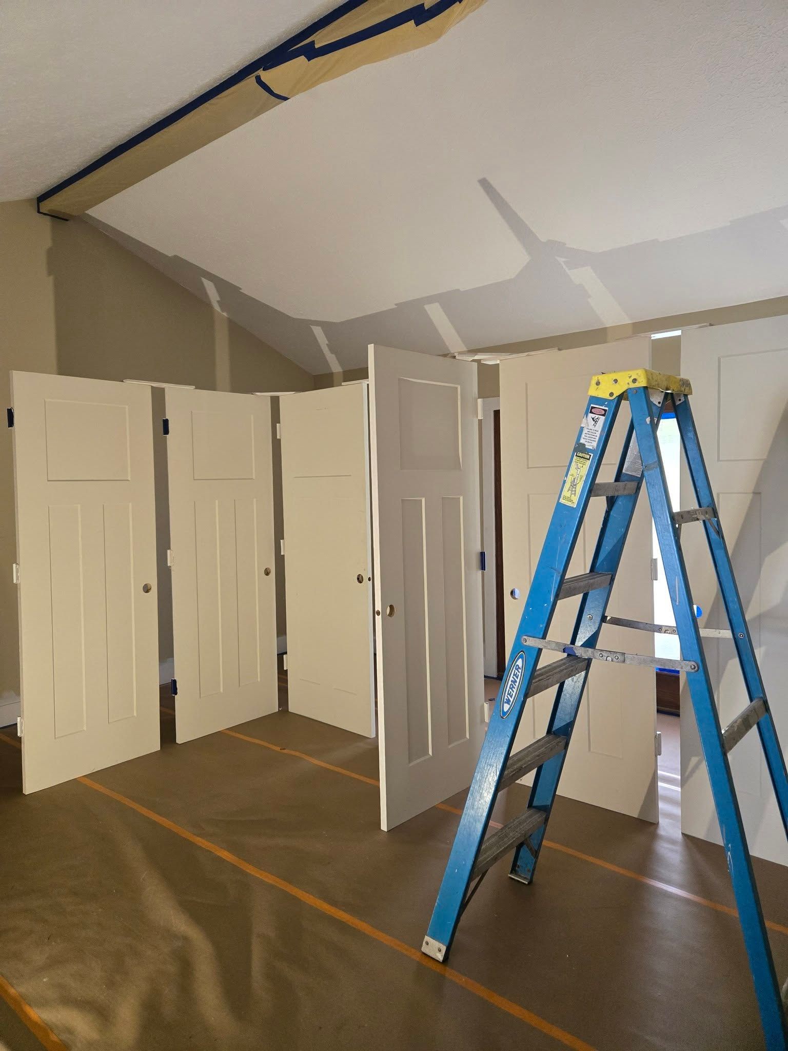 Blue ladder in a room with white closet doors and exposed ceiling patches being repaired