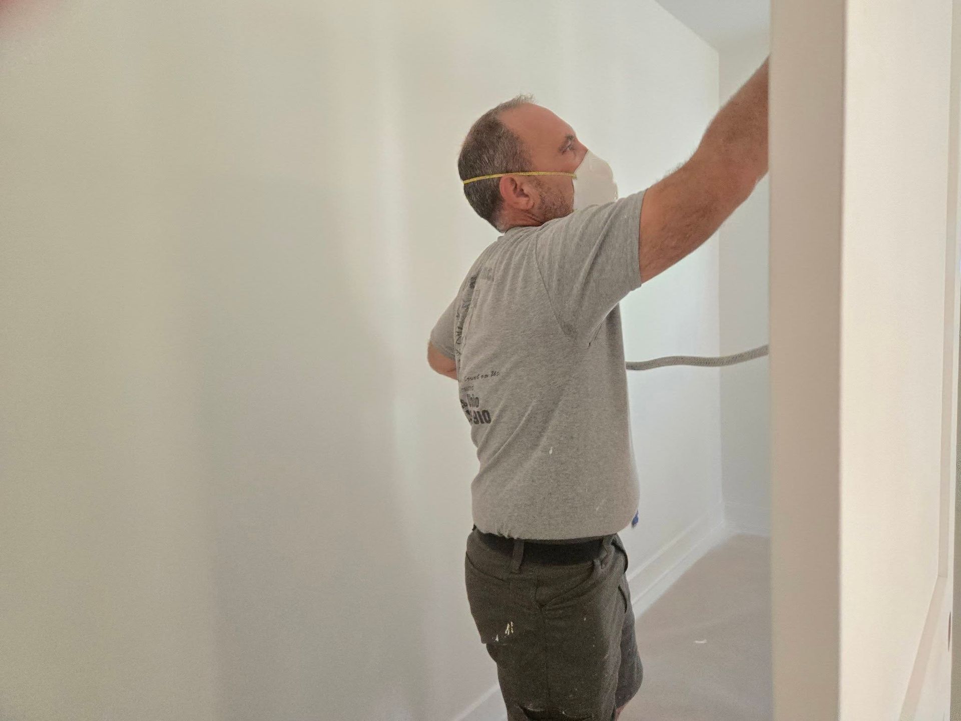 Man in a gray shirt painting a white hallway wall near a doorway.