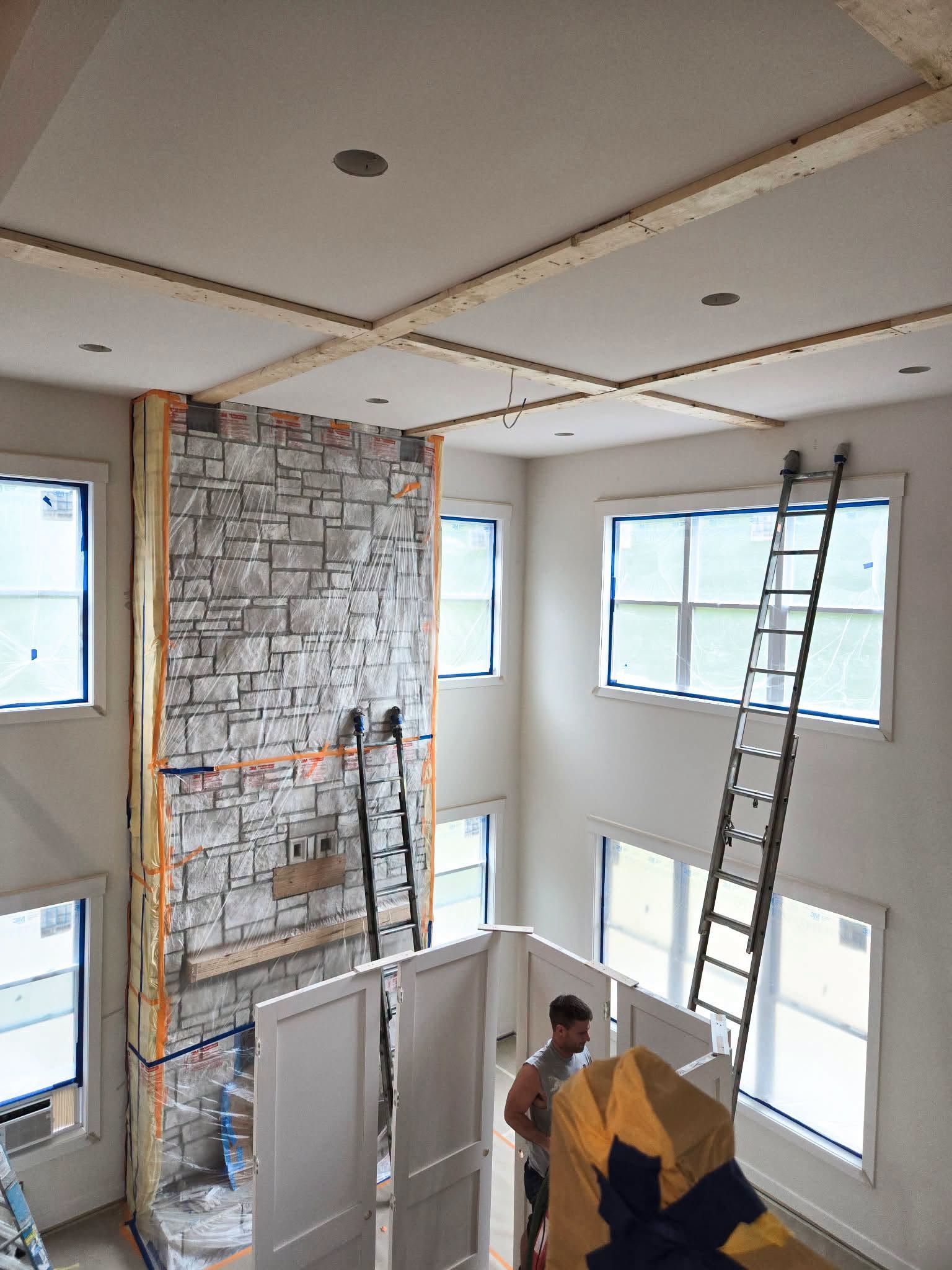 Interior renovation with exposed stone fireplace wall, ladders, and a worker standing below in a bright room