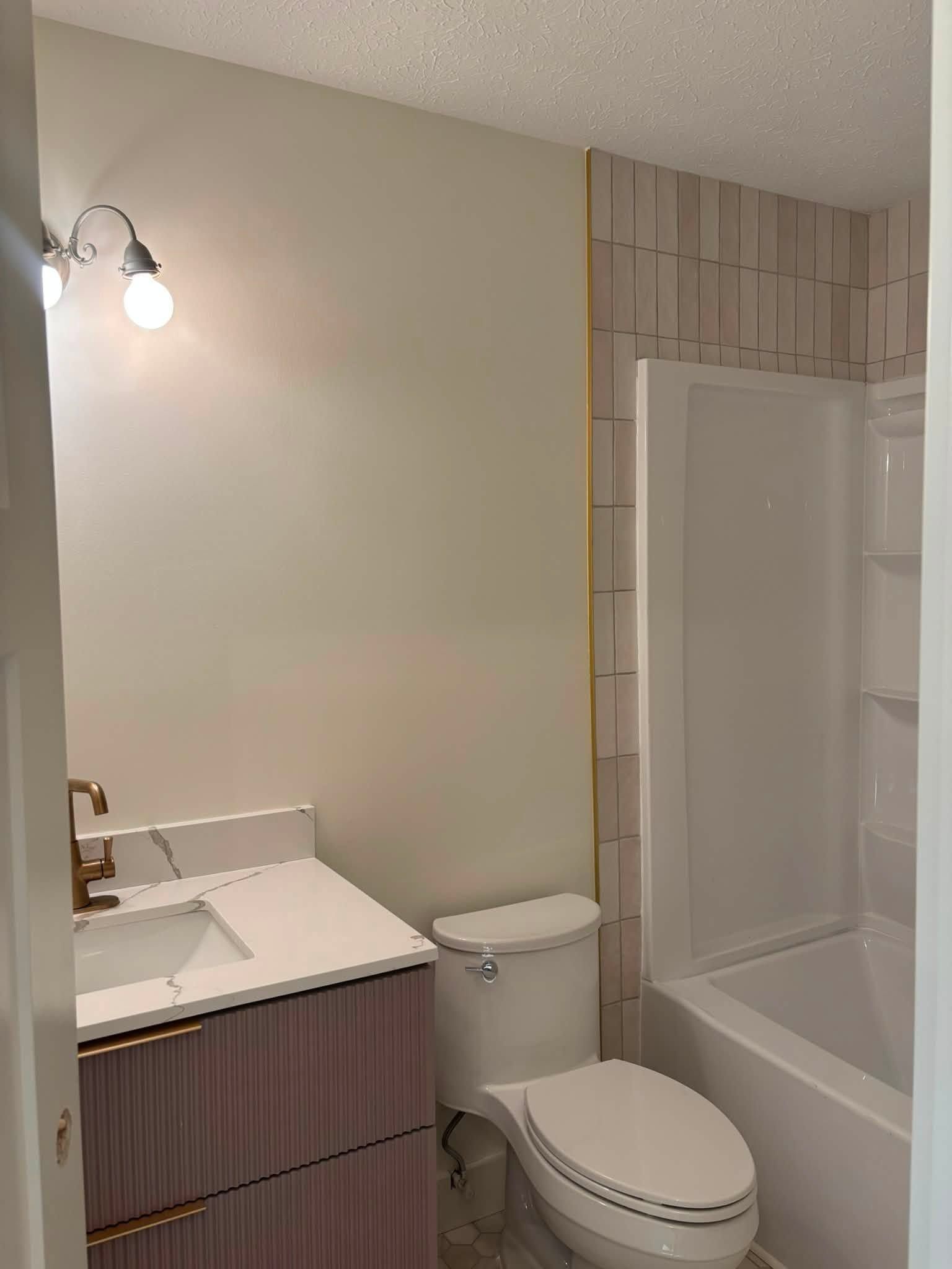 Small bathroom with vanity, toilet, and tub shower with striped tile accents.