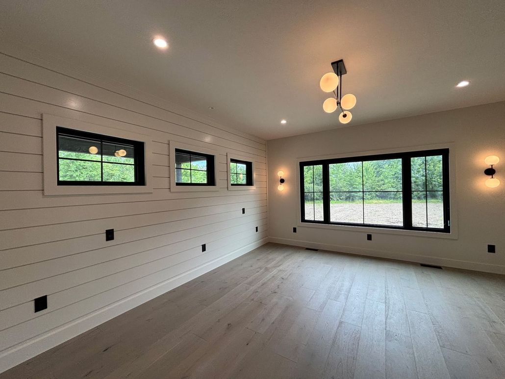 Bright empty living room with white walls, wood floor, black windows, and a modern ceiling light.