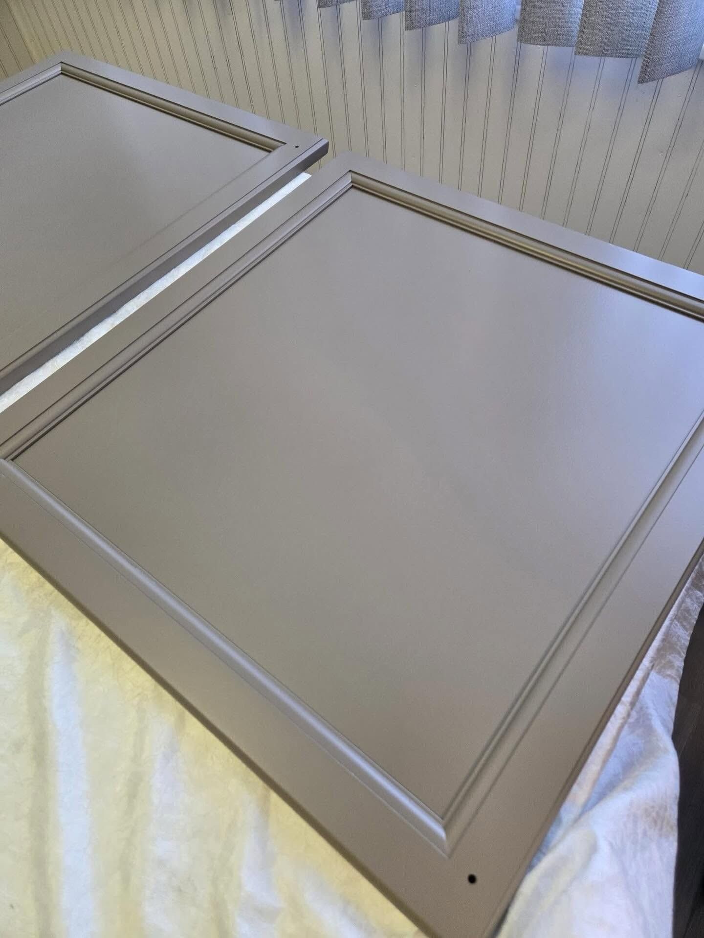 Two beige cabinet doors with silver trim lying on a white cloth￼